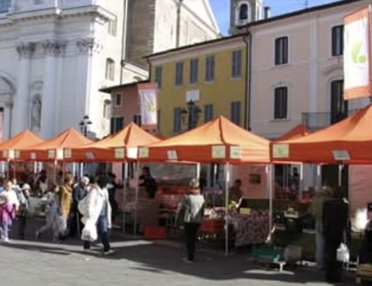 Mercato agricolo con bancarelle arancioni in Piazza Santa Maria a Montichiari.