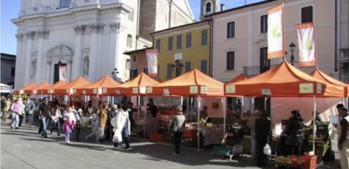 Mercato agricolo con bancarelle arancioni in Piazza Santa Maria a Montichiari.