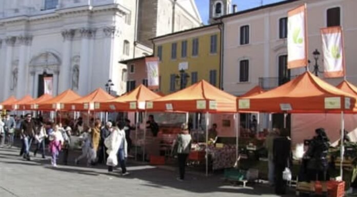 Mercato agricolo con bancarelle arancioni in Piazza Santa Maria a Montichiari.