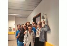 Un gruppo di persone sorride in un corridoio di un ospedale mentre una donna in camice bianco tiene uno stetoscopio
