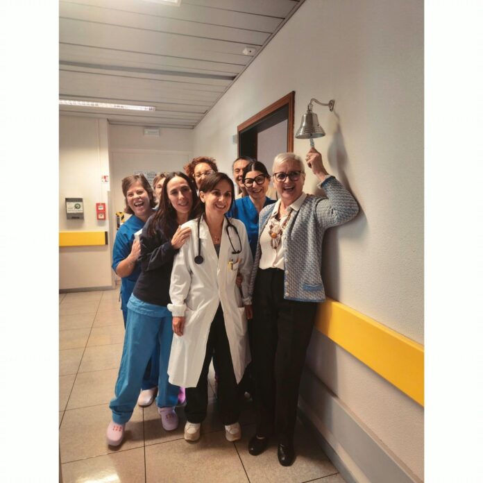 Un gruppo di persone sorride in un corridoio di un ospedale mentre una donna in camice bianco tiene uno stetoscopio