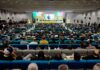 Scena di una grande sala con pubblico seduto davanti a un palco dove un uomo parla