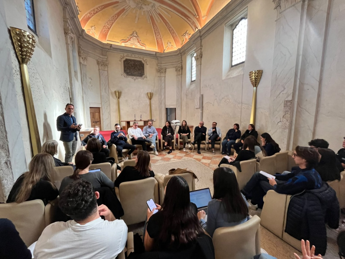 Capitale della Cultura 2029: gli studenti dell'Università di Trento progettano nuove idee per Bardolino 1 Un gruppo di giovani è riunito nella Sala della Disciplina di Bardolino davanti a un palco rosso