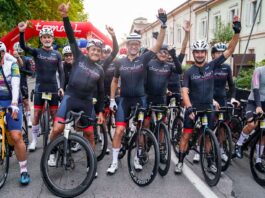 Granfondo Dorelan ReActive a Peschiera del Garda: 1.500 ciclisti da 20 nazioni Un gruppo di persone in abbigliamento sportivo con caschi, in piedi su biciclette, con un'insegna rossa alle spalle.