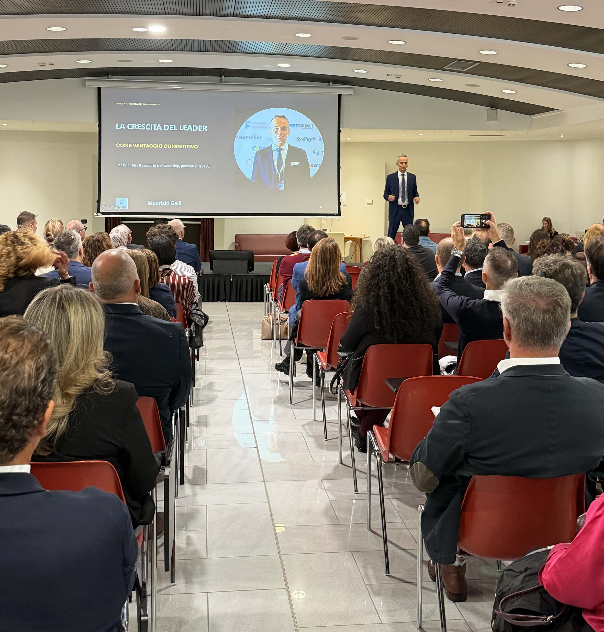 Lake Garda Hospitality Summit a Peschiera del Garda: oltre 500 presenze alla sesta edizione 1 Scena di conferenza con pubblico in sala e figura in piedi davanti a schermo per il Lake Garda Hospitality Summit al Parc Hot