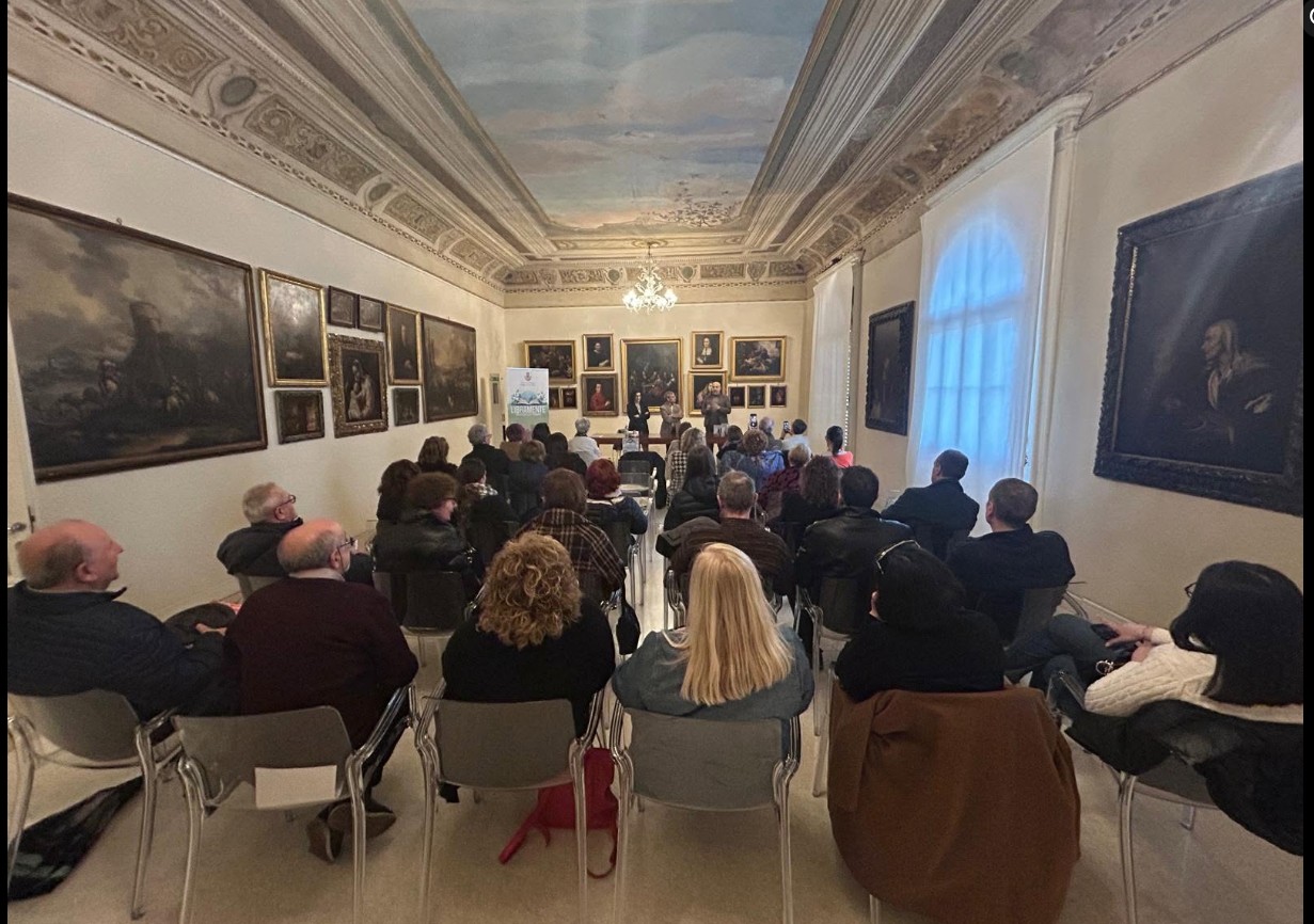 Pubblico in una sala con quadri durante un incontro con l'autore