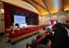 Scena di aula con pubblico seduto e atleti in piedi davanti a schermo per premiazioni a Bardolino