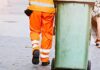 Persona in uniforme trasporta contenitore su strada in contesto servizio raccolta rifiuti