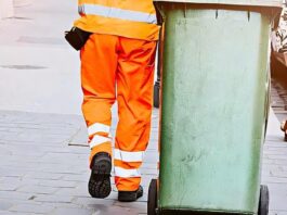 Persona in uniforme trasporta contenitore su strada in contesto servizio raccolta rifiuti