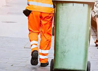 Persona in uniforme trasporta contenitore su strada in contesto servizio raccolta rifiuti