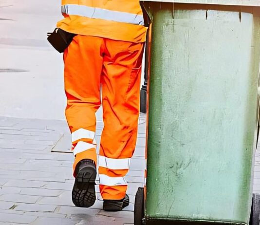 Persona in uniforme trasporta contenitore su strada in contesto servizio raccolta rifiuti