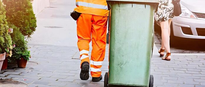 Persona in uniforme trasporta contenitore su strada in contesto servizio raccolta rifiuti